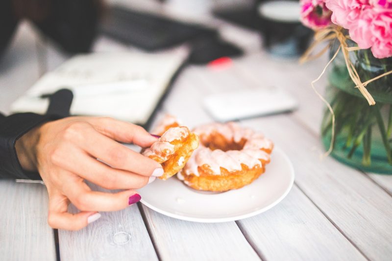 eating glazed donut on white plate on wooden table with flowers