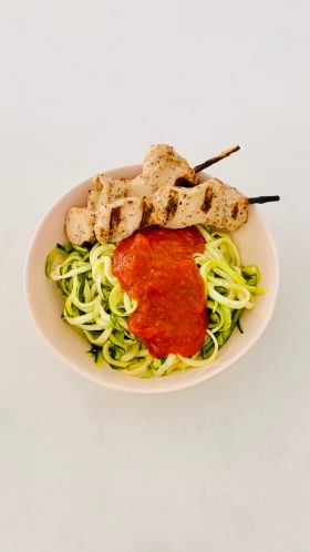 zoodles in white bowl with marinara and grilled chicken on skewer
