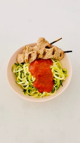 zoodles in white bowl with marinara and grilled chicken on skewer