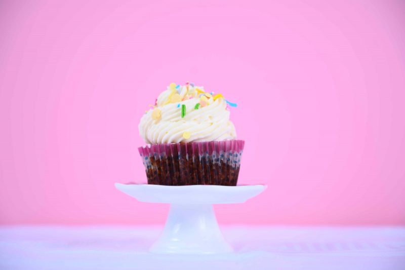 cupcake with vanilla frosting and sprinkles pink background