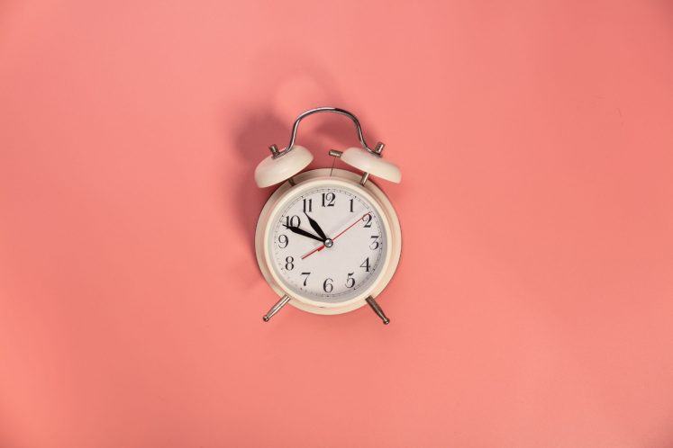 White alarm clock on pink background - flat lay