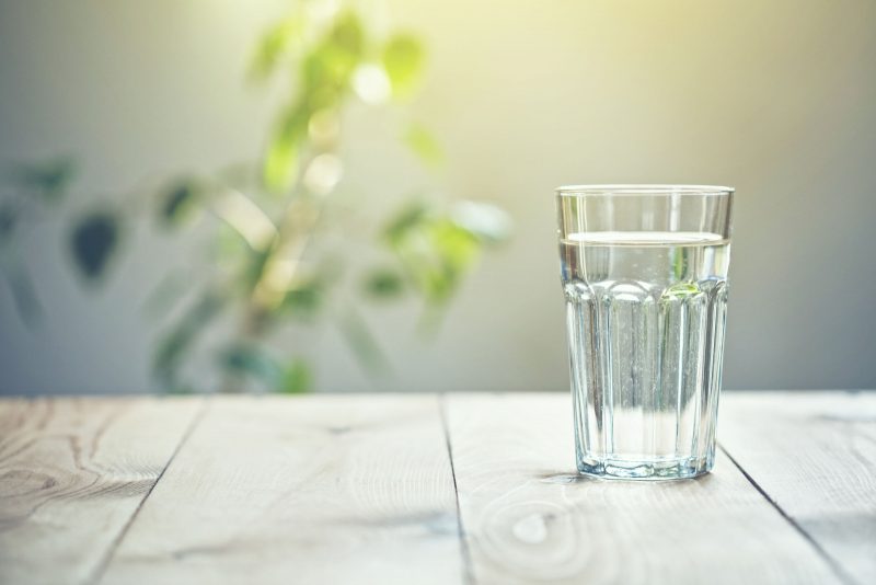 glass of water on table with plant in background
