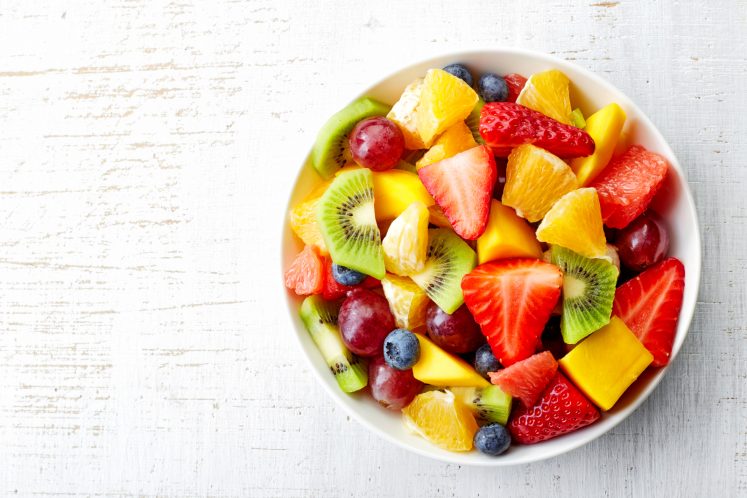 healthy bowl of cut fruit on white surface