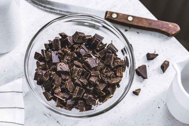 dark chocolate chopped in a glass bowl on a white counter