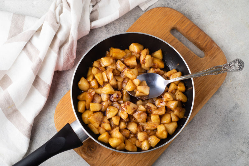 image of an easy healthy dessert recipe, pan of warm sauteed cinnamon apples, with silver spoon