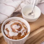 cinnamon roll baked oats mug cake in white ramekins with drizzled icing