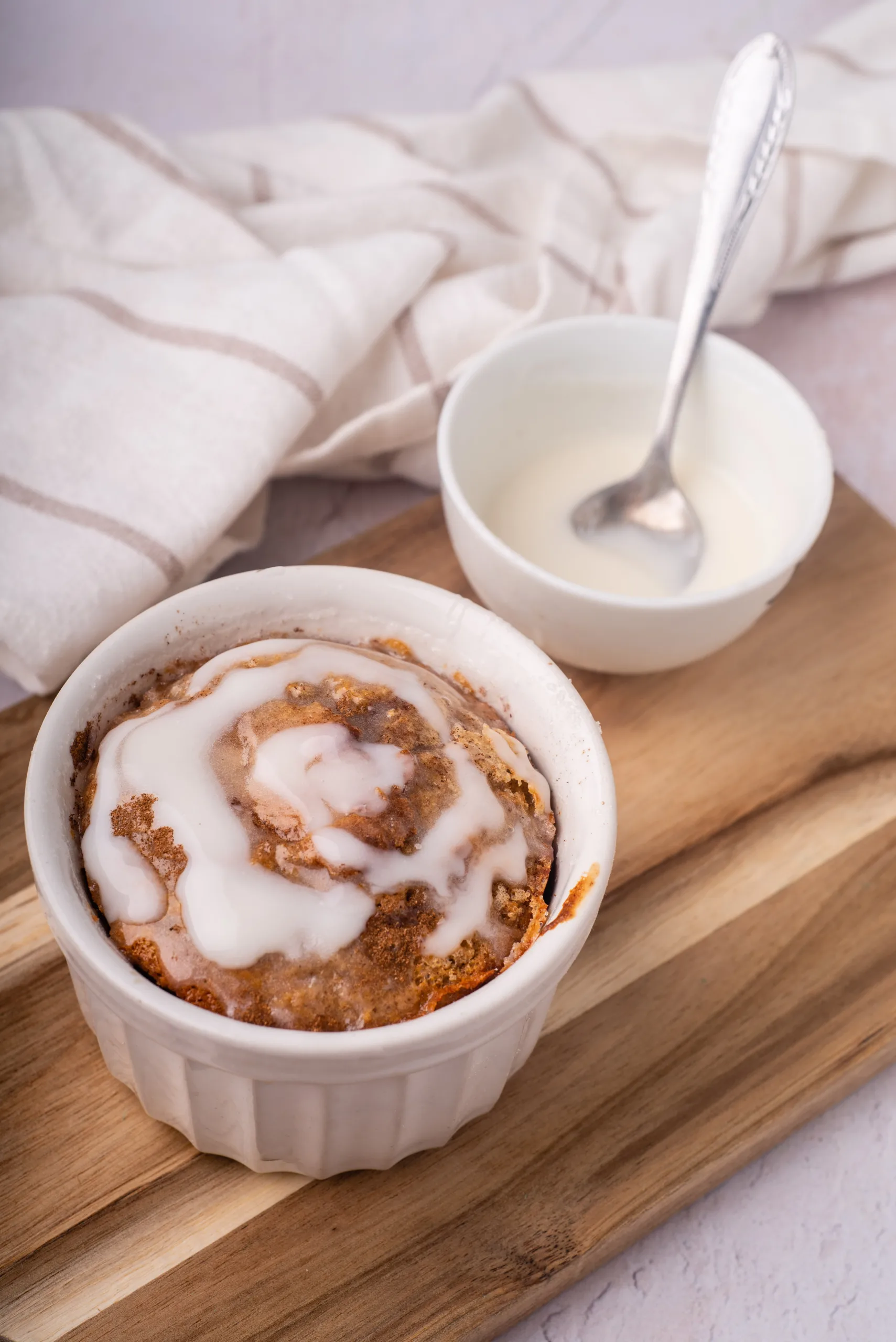 cinnamon roll baked oats mug cake in white ramekins with drizzled icing