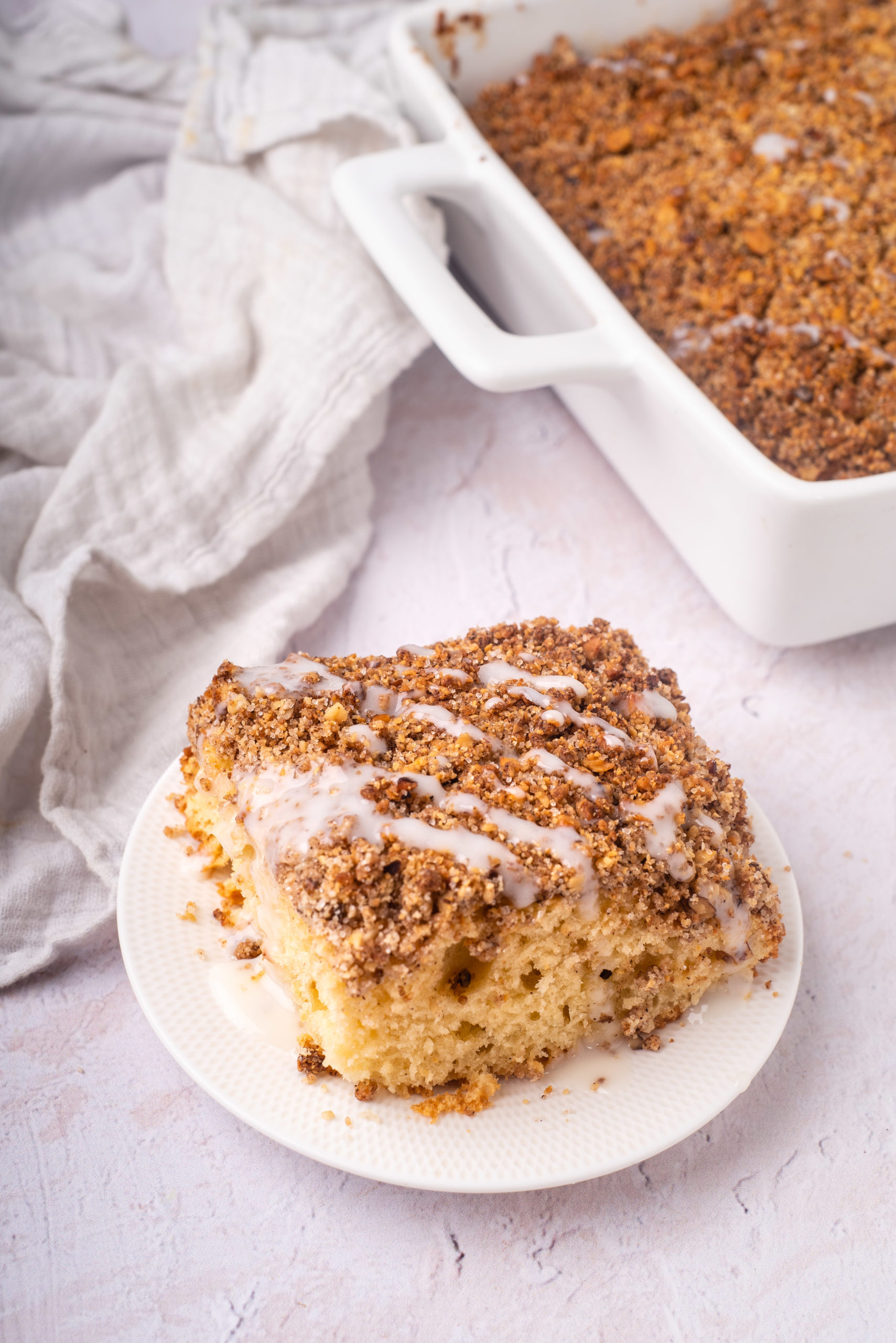 slice of gluten and dairy free cinnamon coffee cake with streusel and sugar free glaze on white plate with whole cake in background