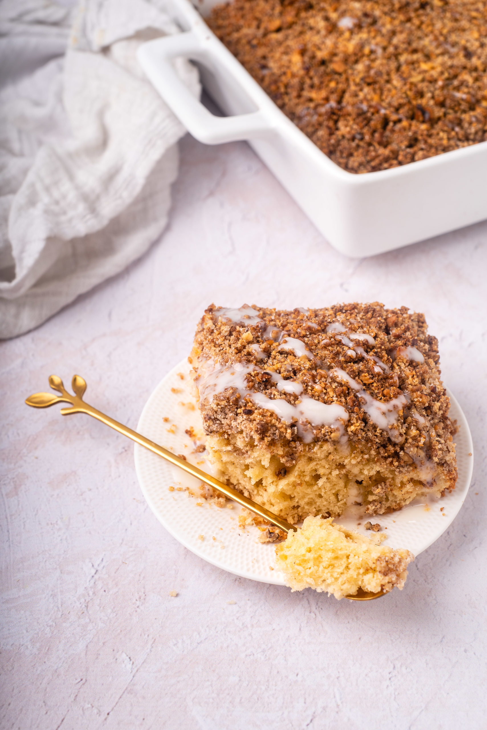 slice of gluten and dairy free cinnamon coffee cake with streusel and sugar free glaze on white plate with bite on a fork