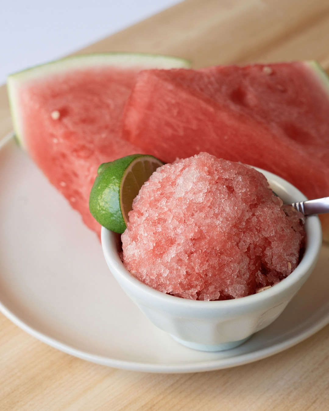 closeup watermelon slushie in small white bowl with watermelon wedges in background