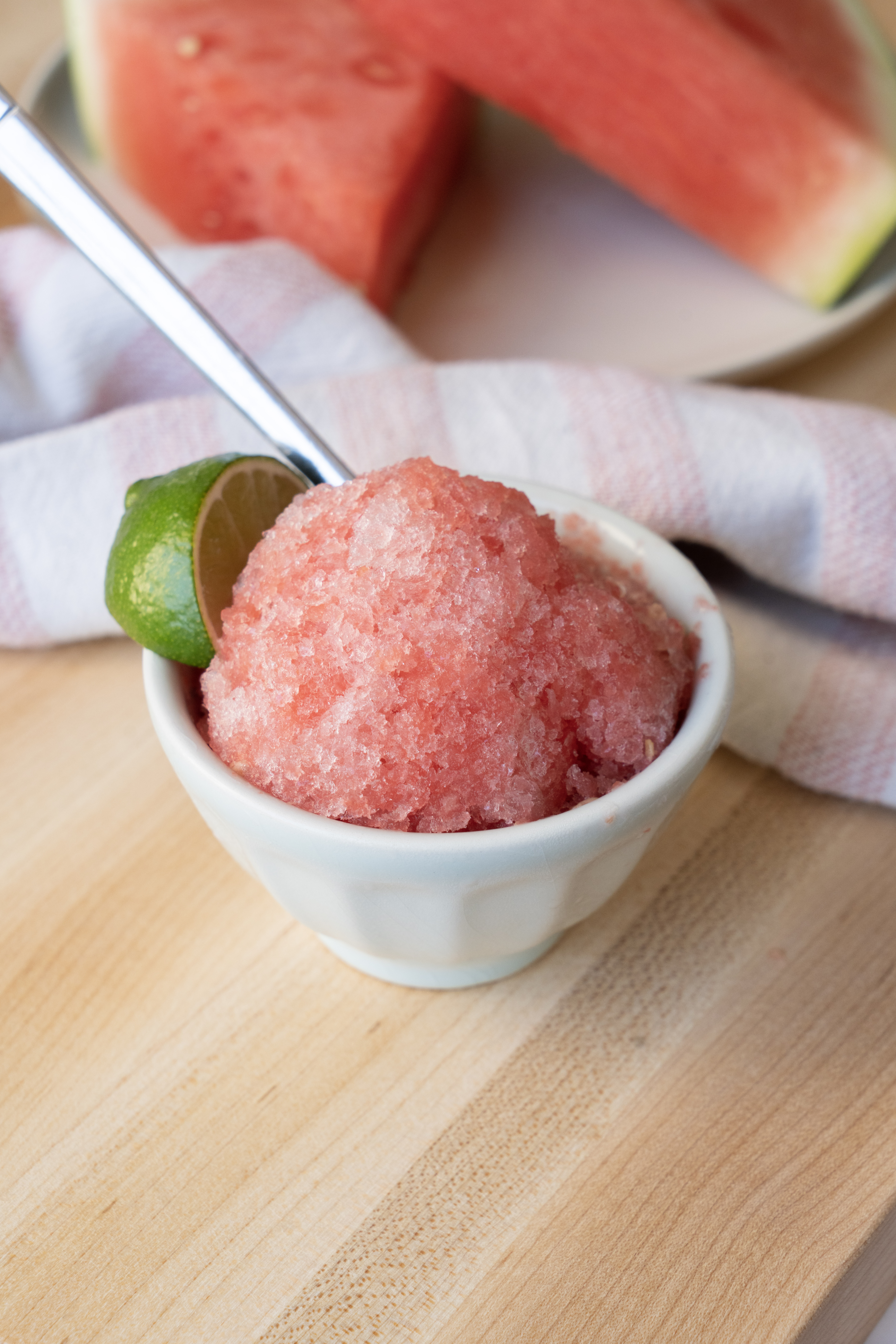 watermelon slushie in small white bowl with lime on butcher block