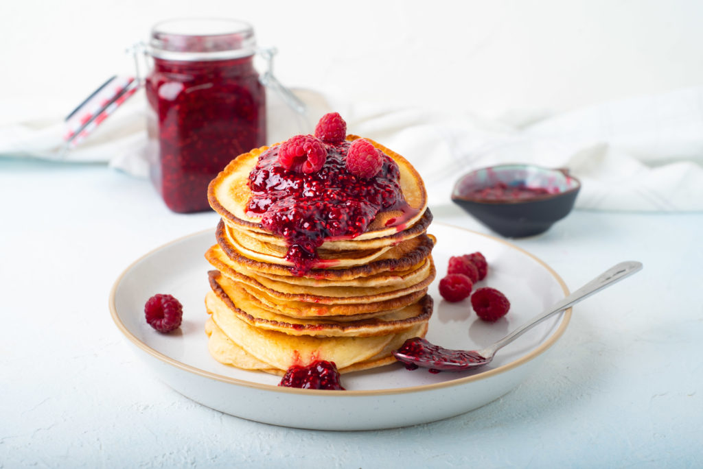 stack of pancakes with blogilates raspberry chia jam on top, dripping down side