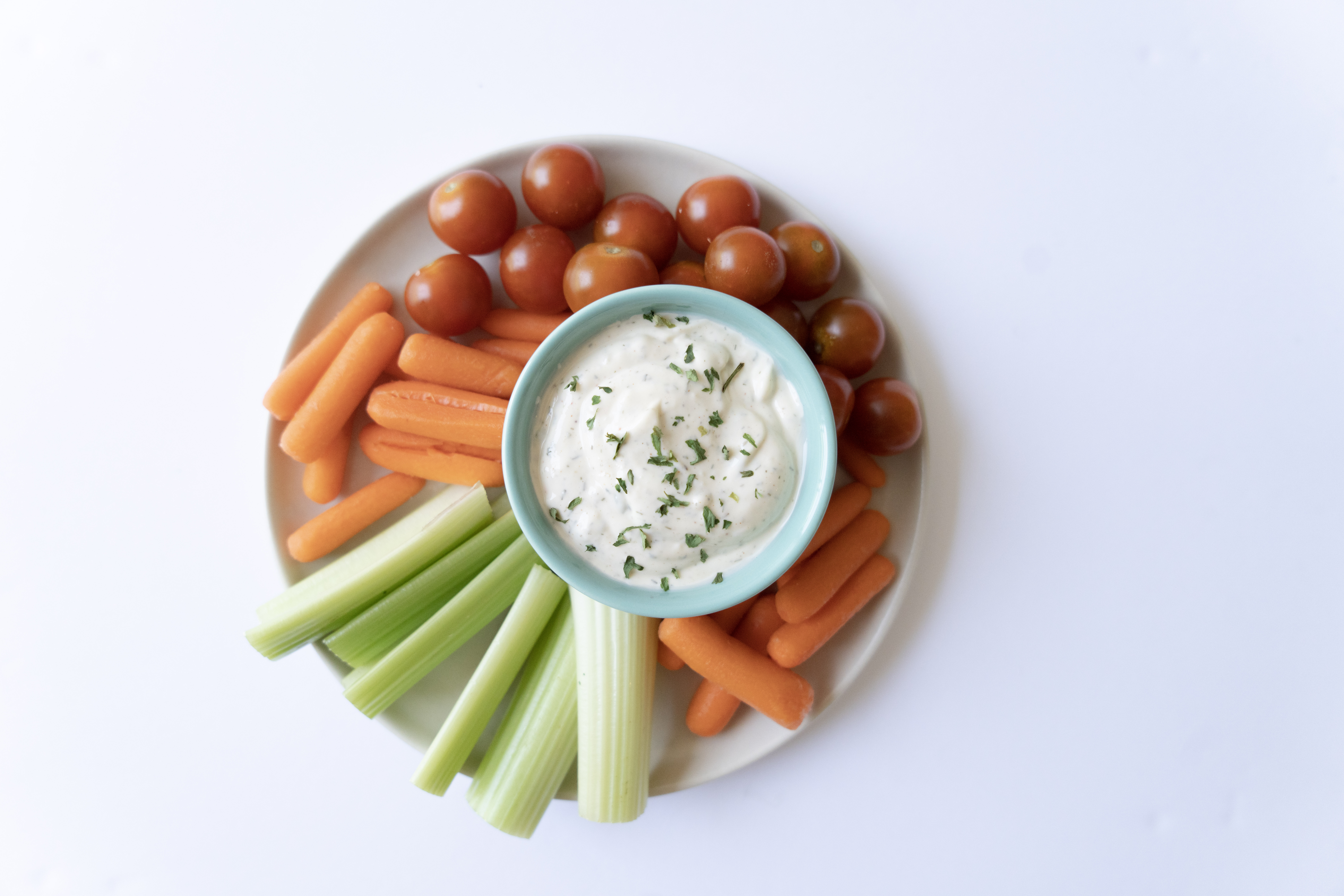 plate with bowl of dairy free ranch with chives served with carrots celery and tomatoes