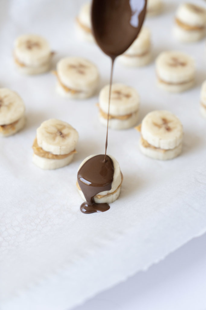spoon drizzling chocolate on peanut butter banana bites