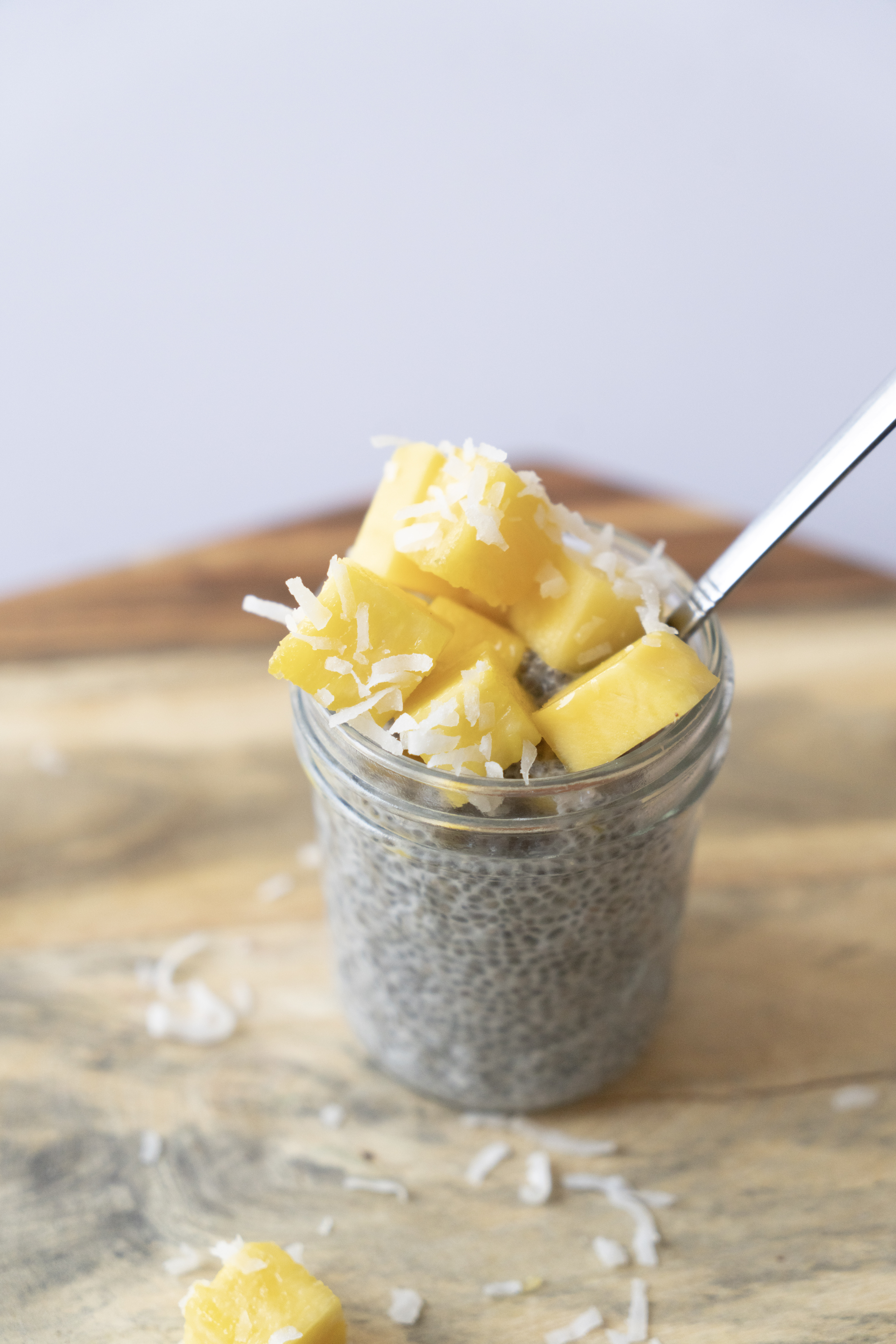 chia pudding with tropical fruit and coconut in a jar with a spoon on cutting board