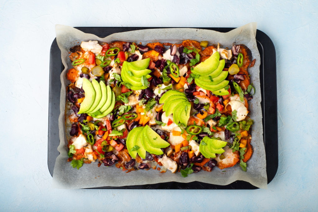 sweet potato nachos topped with beans jalapeno salsa avocado on a sheet pan