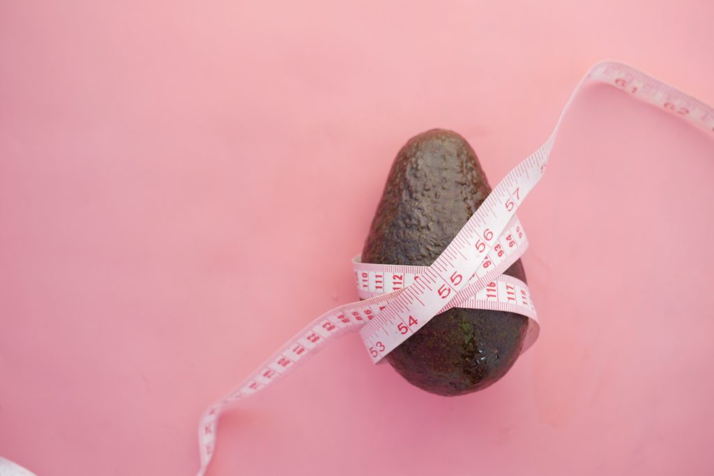 avocado wrapped in measuring tape on a pink background crash dieting