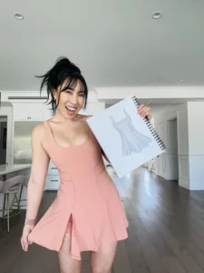 Cassey Ho wearing the terracotta Superdress holding up the original workout dress sketch