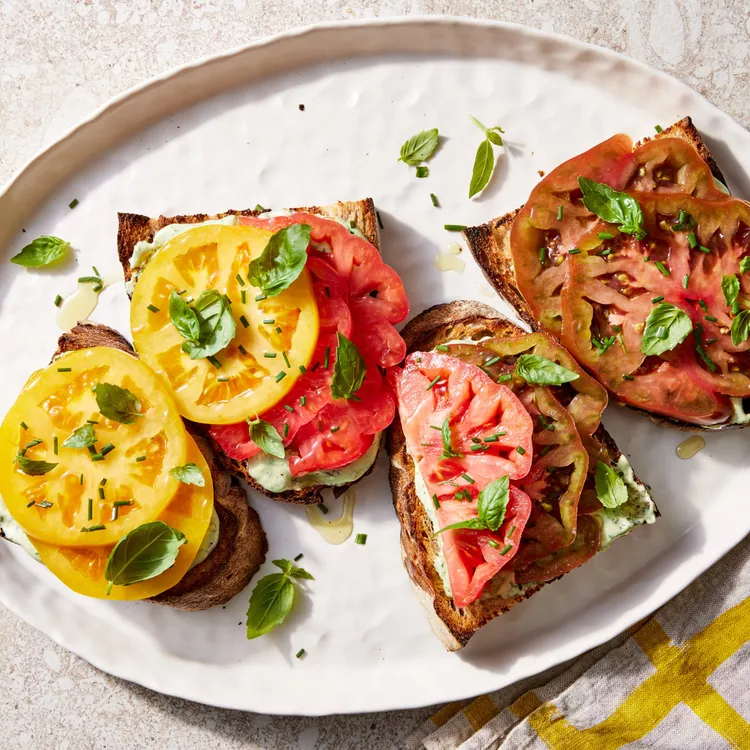 ricotta and tomato toast on a white plate sprinkled with herbs
