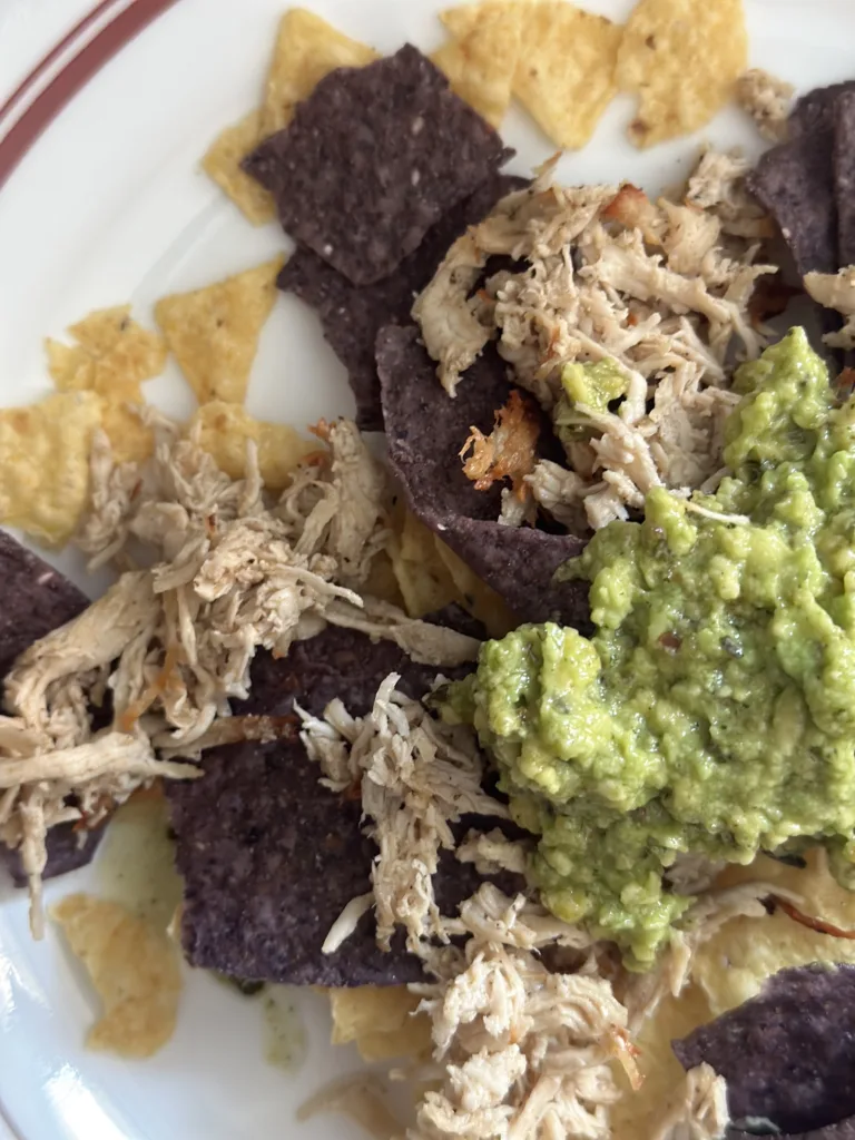 plate of nachos with chips, guacamole and shredded chicken girl dinner